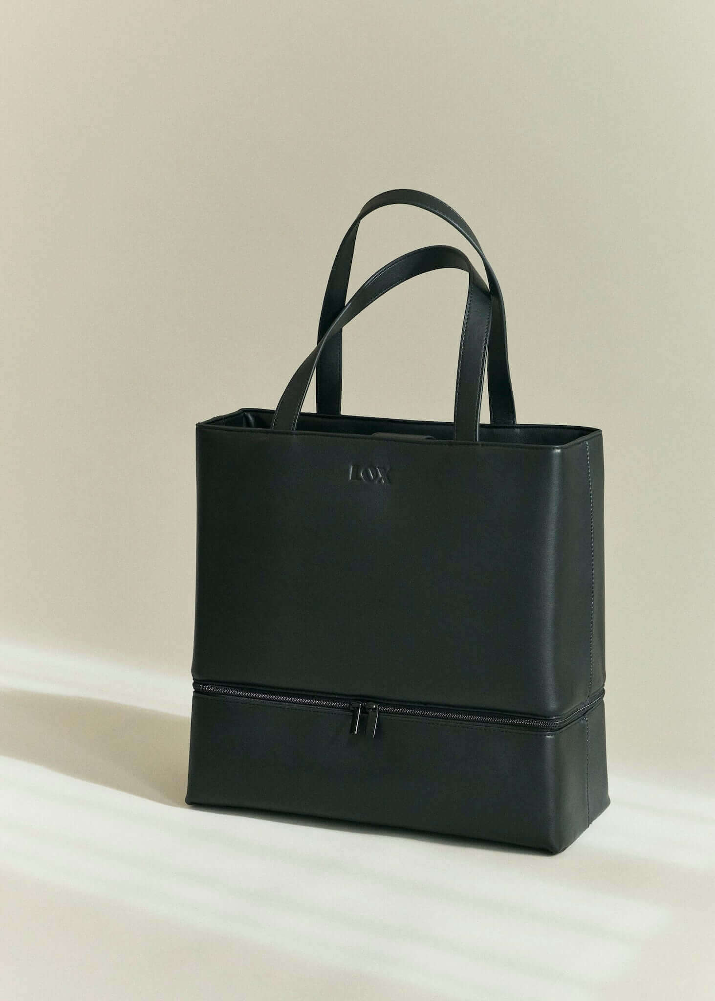 black vegan leather bag, sitting on a tonal cream studio floor bathed in sunlight