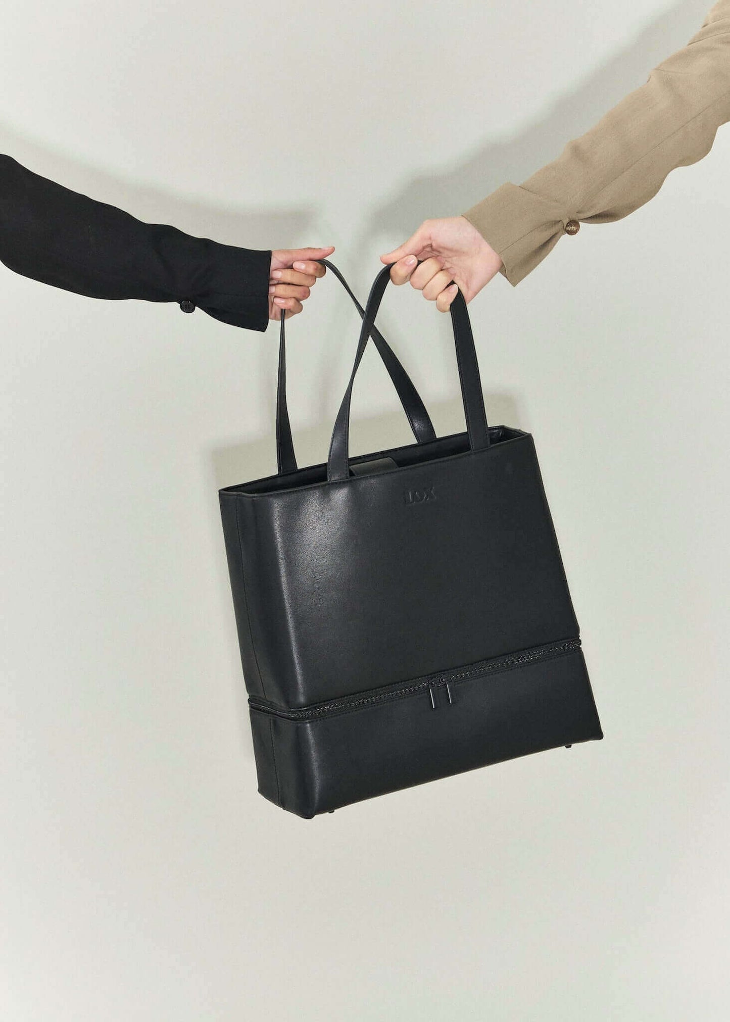 black vegan leather bag being held by two female hands, signifying friendship