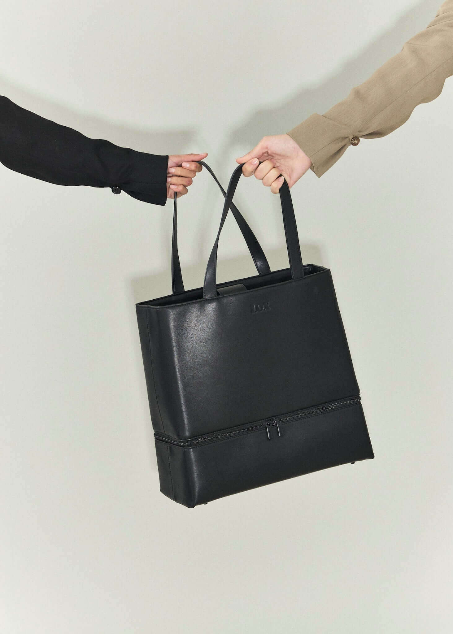 black vegan leather bag being held by two female hands, signifying friendship